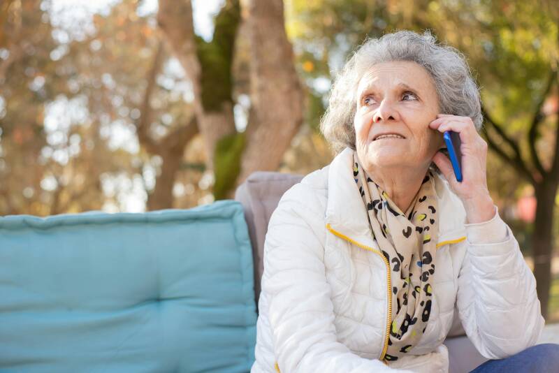 Older woman with gray hair sitting outdoors talking on a cell phone