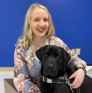 Smiling blonde woman holding a black Labrador dog
