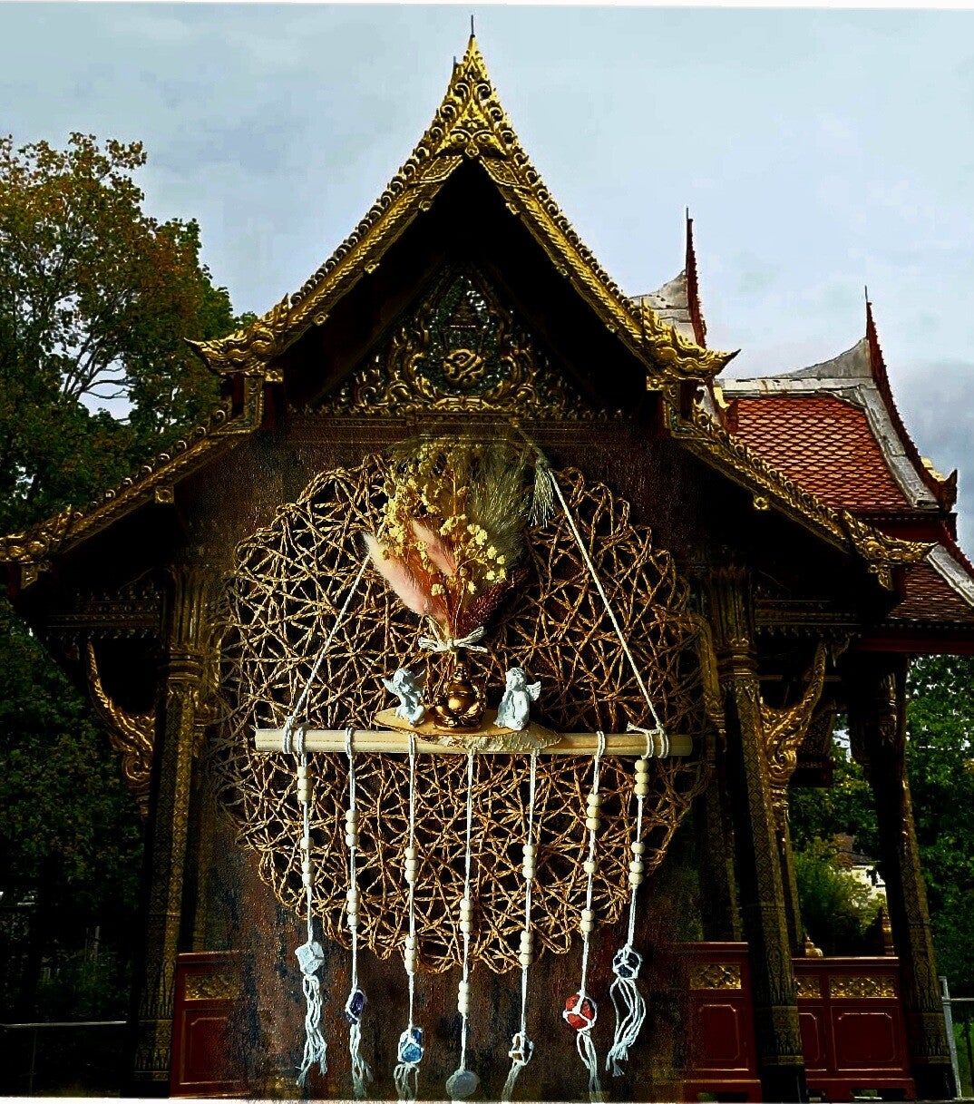 Selbst gemachter Traumfänger mit Engeln, Buddha, Trockenblumen und Heilsteinen. Im Hintergrund ein Tempel in Bad Homburg.