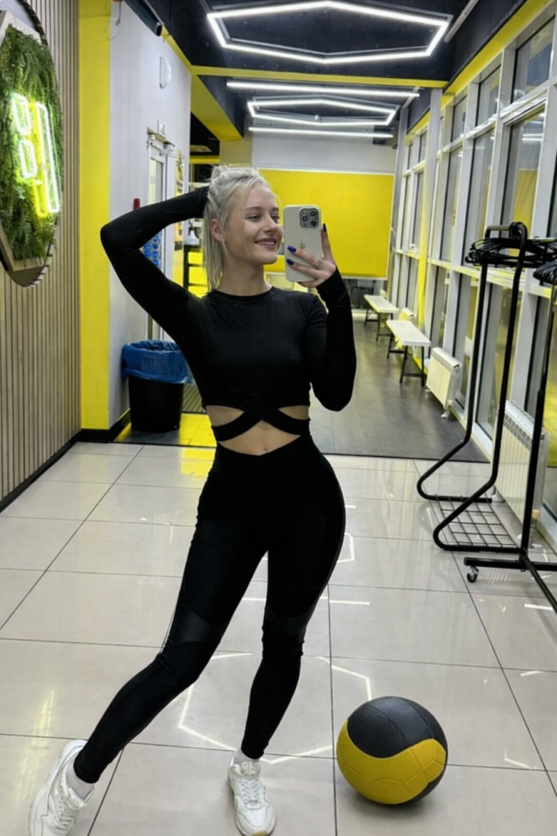 Sportliches blondes Model Hole in 2 im Gym mit Medizinball und langen Haaren – athletischer Look beim Training