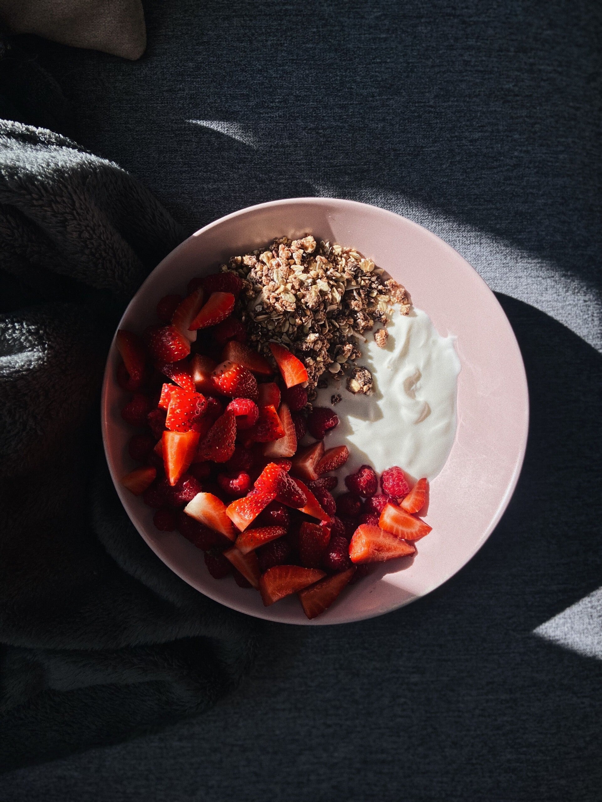 Roze bord met ontbijtgranen, yoghurt en vers fruit.