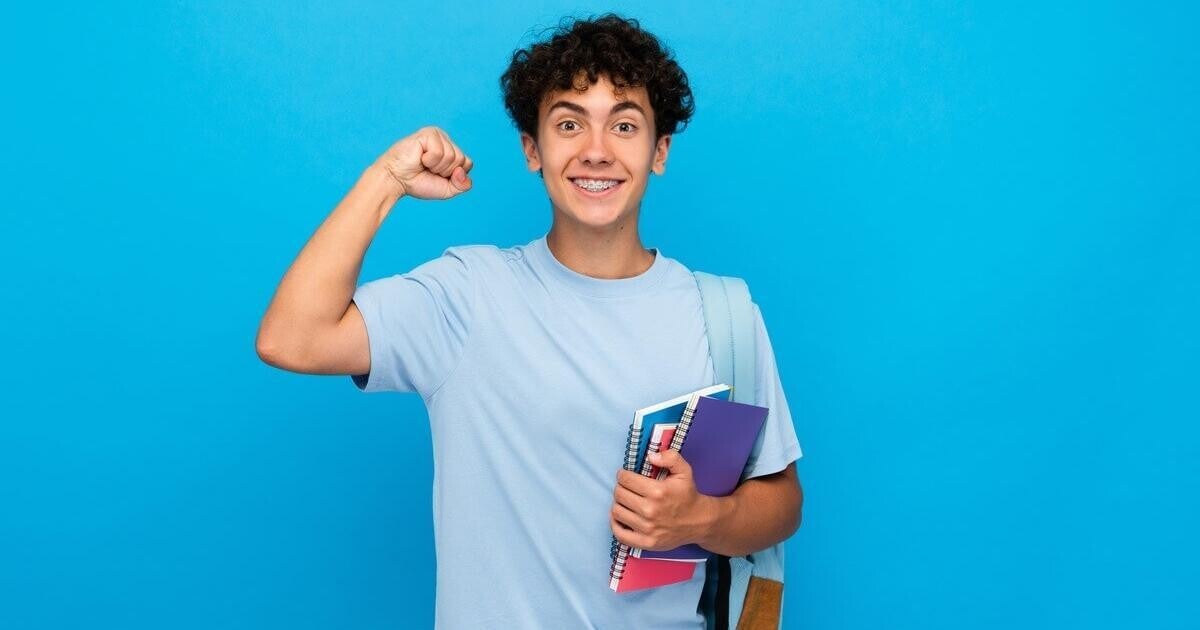Happy and confident teenage boy carrying school books, representing resilience, self-belief, emotional wellbeing, motivation, and positive personal growth for young men.