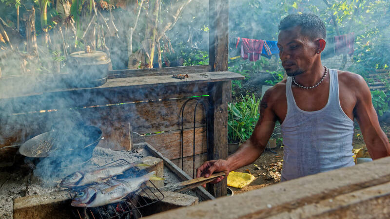 A young man is grilling fish in kampung Rumaat, Kai Kecil, Maluku Tenggara, Indonesia  © Perrin Oubrie Photography