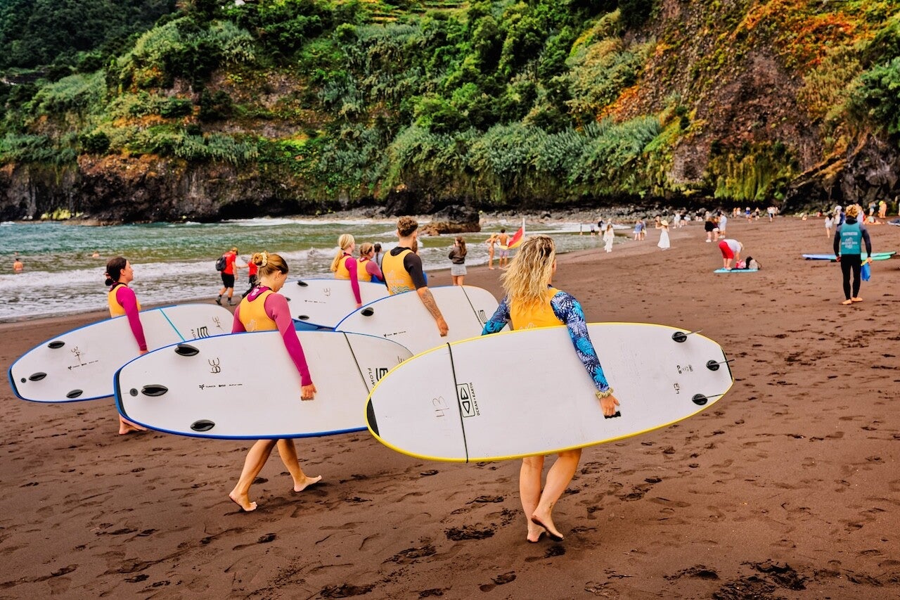 Surf School students are walking with their boards on Seixal Beach to start their first lesson