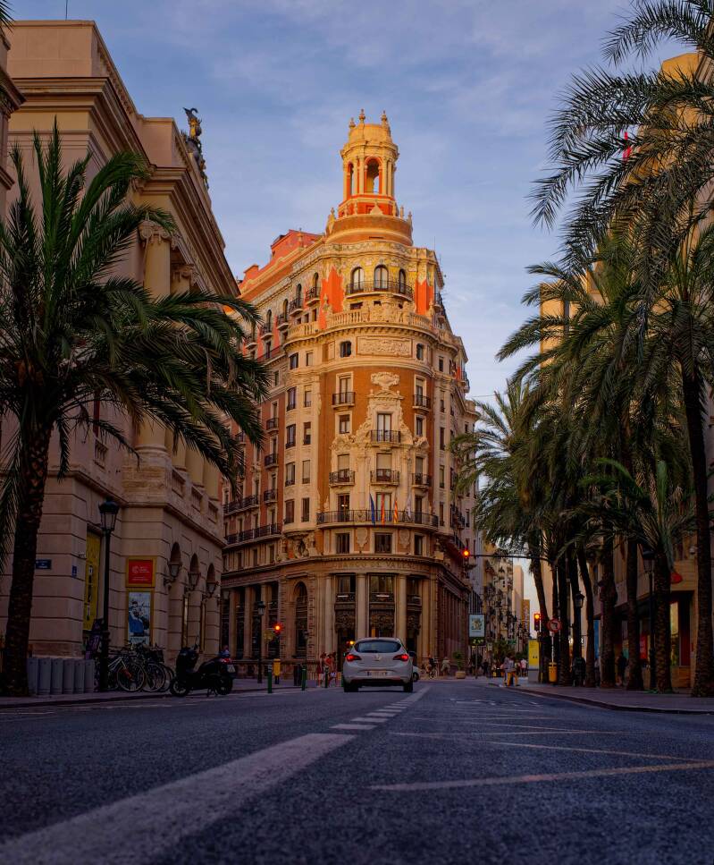 A low angle street view of the Banco de Valencia building with palm trees on the side