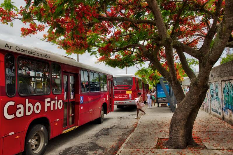 A woman carrying a baby is getting on the bus at the bus stop in Cabo Frio, Rio de Janeiro, Brazil