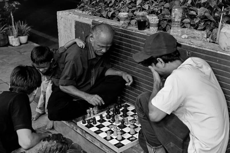 A street photo of men playing chess outside on the pavement in Labuan Bajo, Flores, Indonesia