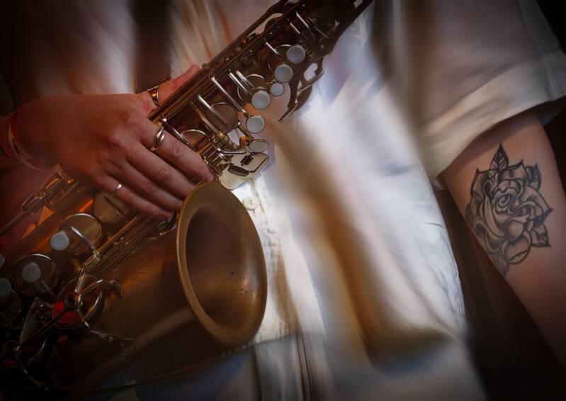 Art photo of jazz musician  Jasmine Myra holding her Saxophone and showing her under arm with a Rose tattoo during a live concert 