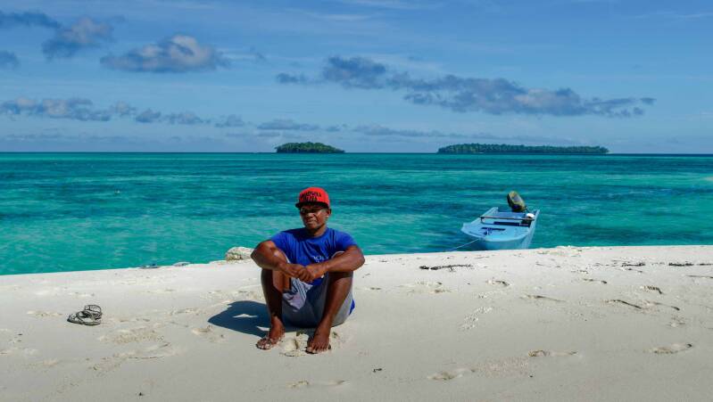 A photo of a man sitting on a white sandy beach of Ngur Tafur in the Banda Sea,  Kai Islands, Maluku Tenggara, Indonesia 
