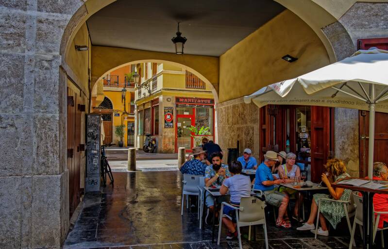 A street photo of people relaxing on a terrace in Placa Redona which is located in the old town of Valencia, Spain
