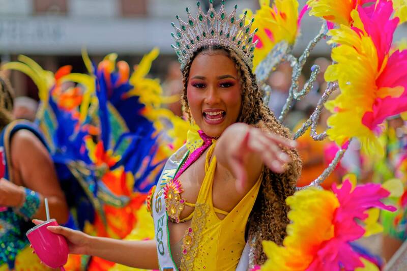 Beautiful Carribean lady is wearing a diamond crown and yellow pink costume is pointing at the camera during the Rotterdam Summer Carnival 2024