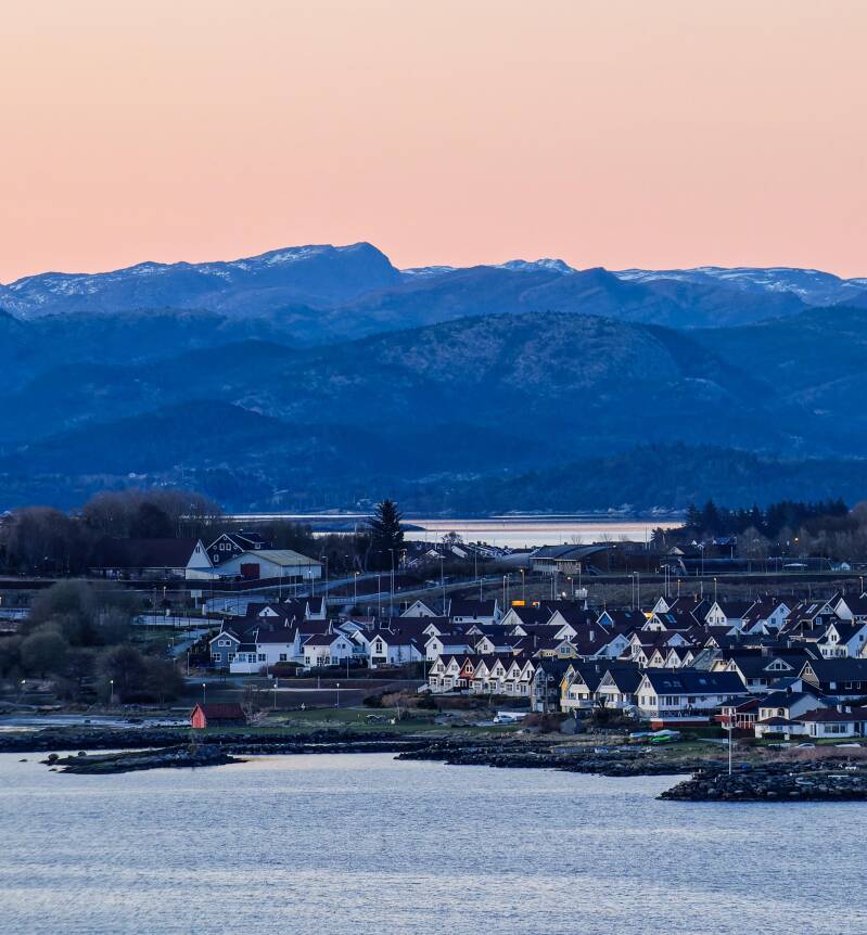 A sunrise photo of the white wooden houses Stavanger, with a backdrop of mountains in Norway  