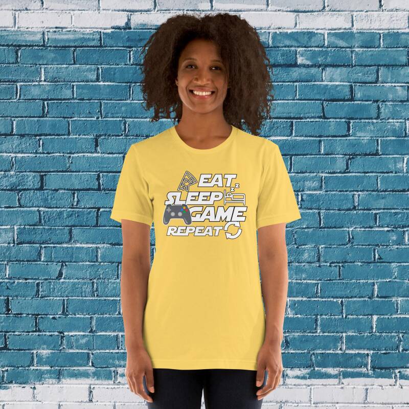 Modelo mujer con camiseta "Eat, Sleep, GAME, Repeat", destacando el mando de consola colorido como pasión gamer.
