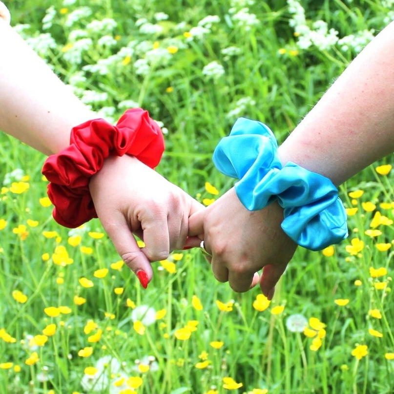 Twee handen die elkaar vasthouden met om de pols een satin scrunchie als modeaccessoire 