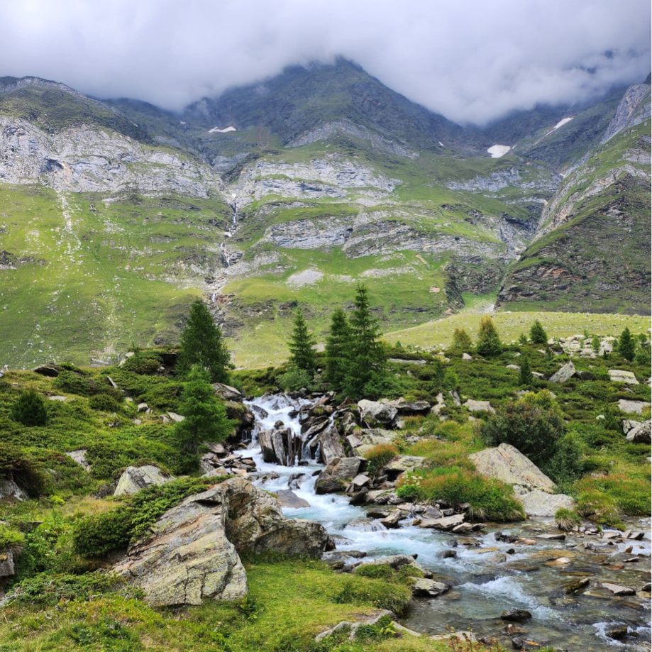 Foto von Berglandschaft, wolkenverhangen und im Vordergrung dein Bergbach