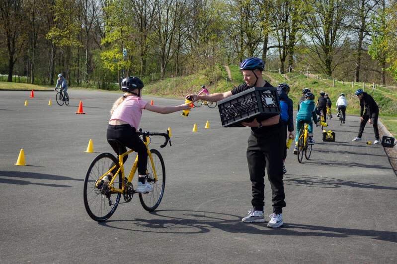 Instructeur Paul van de Ven geeft een bidon aan, waardoor leerlingen kort met één hand los moeten fietsen / Foto: Sven Dimmendaal