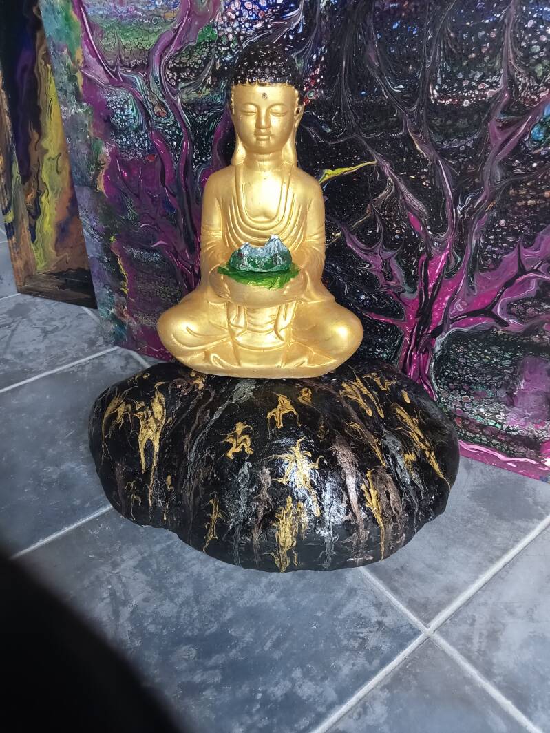 Goldener Buddha Mit kleinen Watzmann am Schoß, Im Hintergrund ein Pouring Bild mit mystischen Bäumen  in Lila Grün Weiß uns Schwarz.