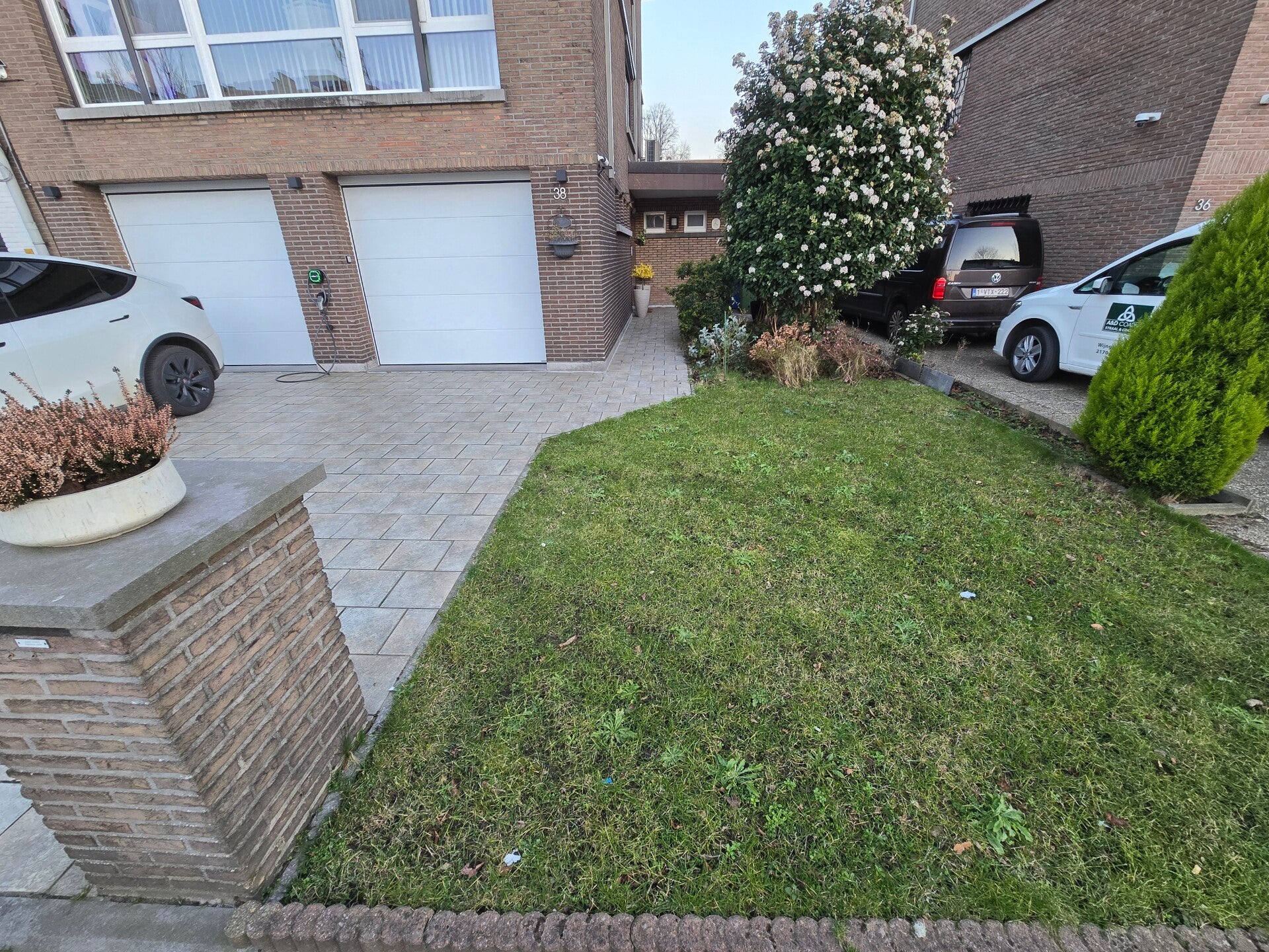Oprit in bruine klinkers naast een aangelegd gazon, met een gemetselde tuinmuur langs de straat.