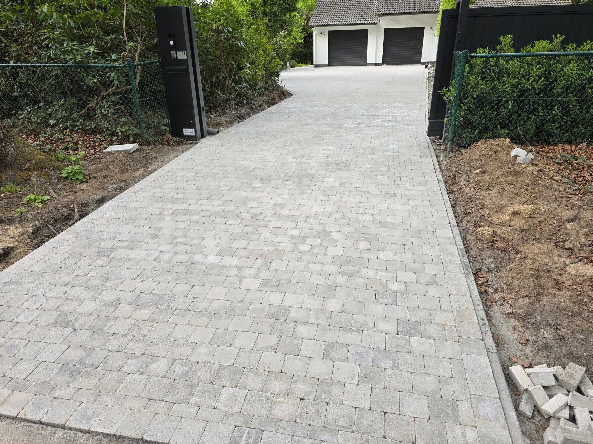 Brede oprit in lichtgrijze klinkers tussen twee garages, strak in halfsteensverband gelegd.