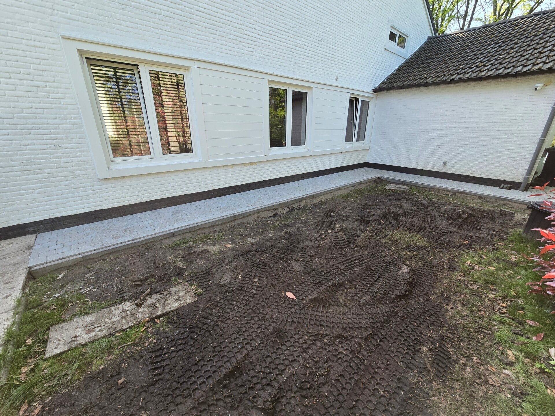 Tuin in aanleg achter een witte woning: het terrein is uitgegraven en geëffend voor nieuw gazon.