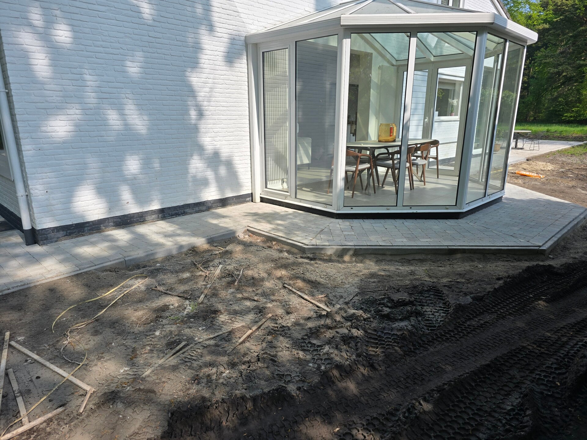 Nieuw terras in lichte tegels rondom een veranda met glazen wanden.
