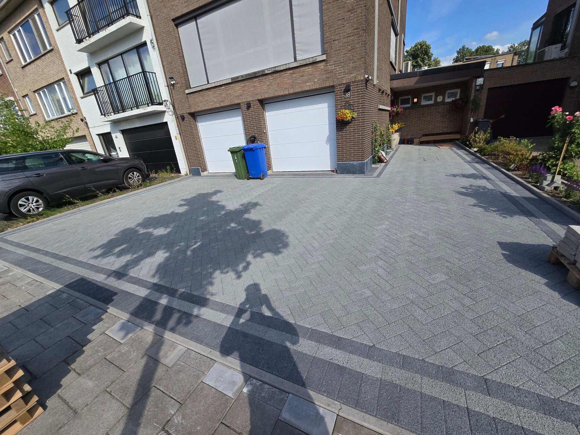 Grote oprit in antracietkleurige klinkers voor een appartementsgebouw, met boordsteen langs het gazon.