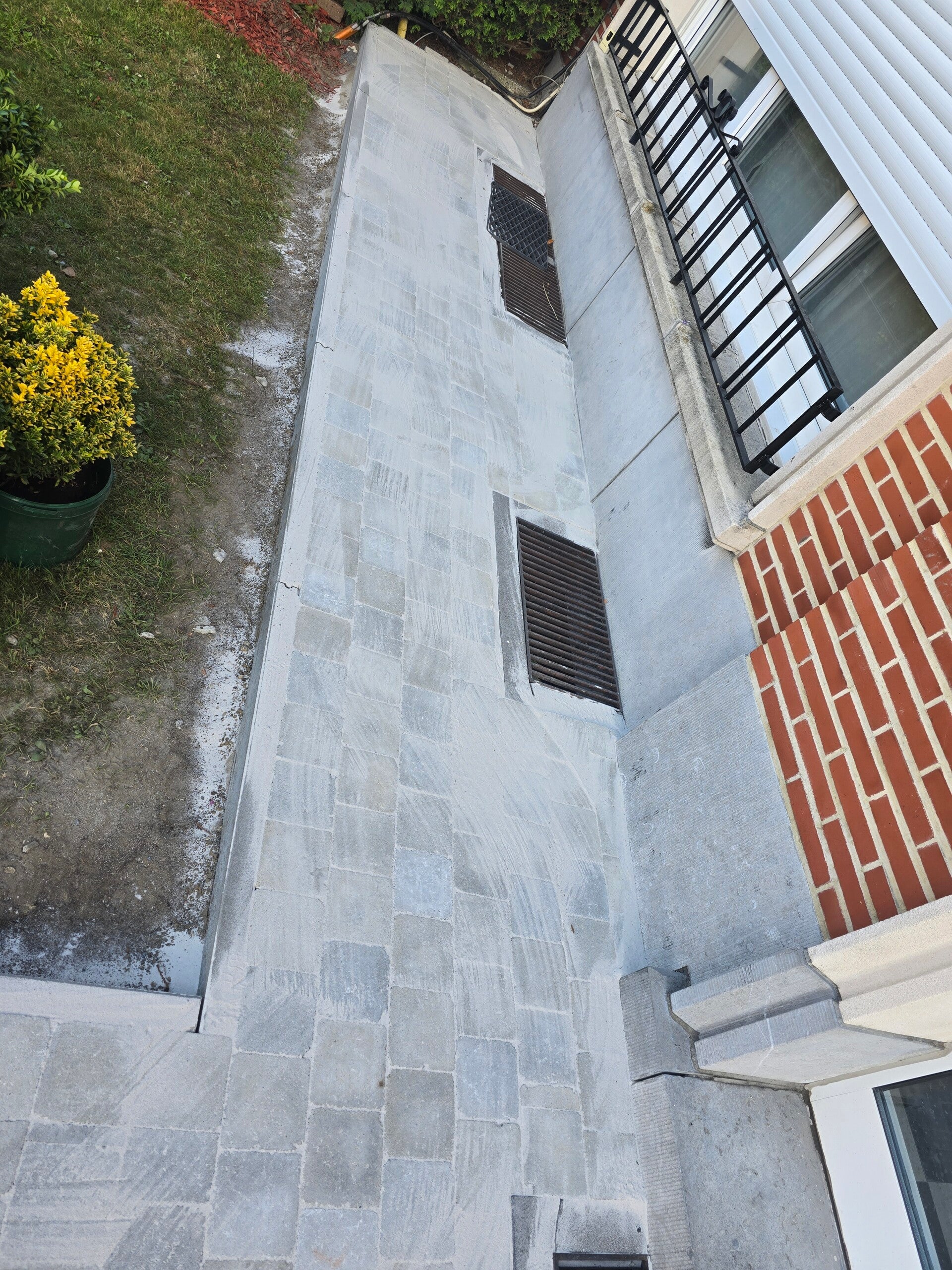Smal tuinpad in witte tegels langs de zijgevel van een woning, met beplanting in potten.
