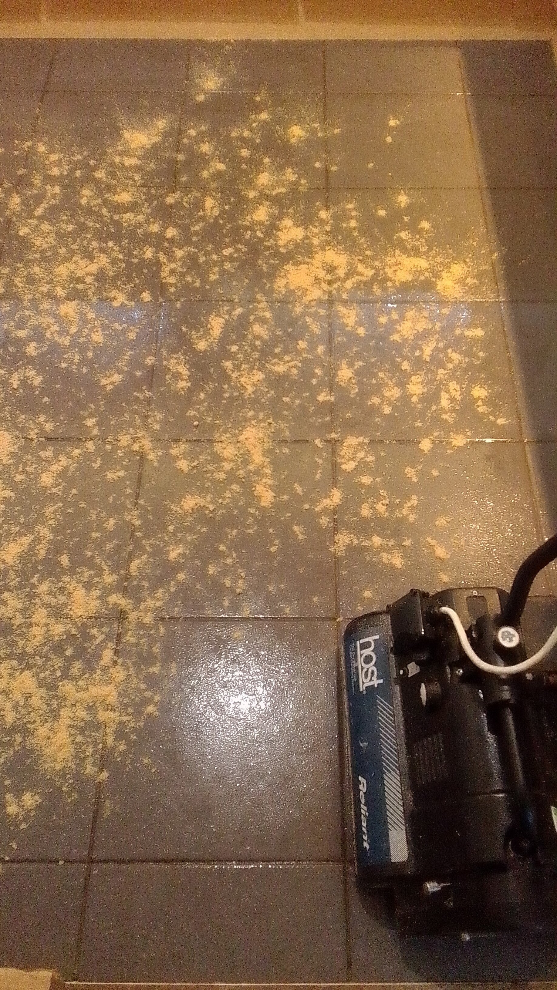 Tiled floor being cleaned using a rotating brushing machine and absorbant granules