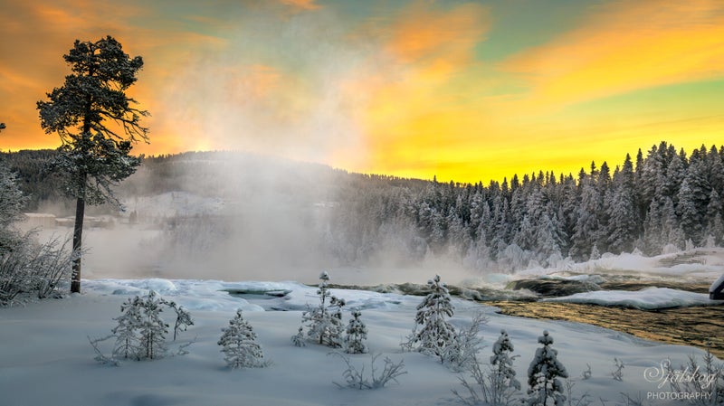 The golden light catching the mist is absolutely beautiful. The frozen cascades and snow-draped surroundings create a magical scene that feels almost otherworldly.