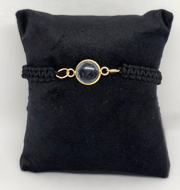 Armband zwartgevlochten koord met goudkleurige bedel gevuld met zwarte epoxy