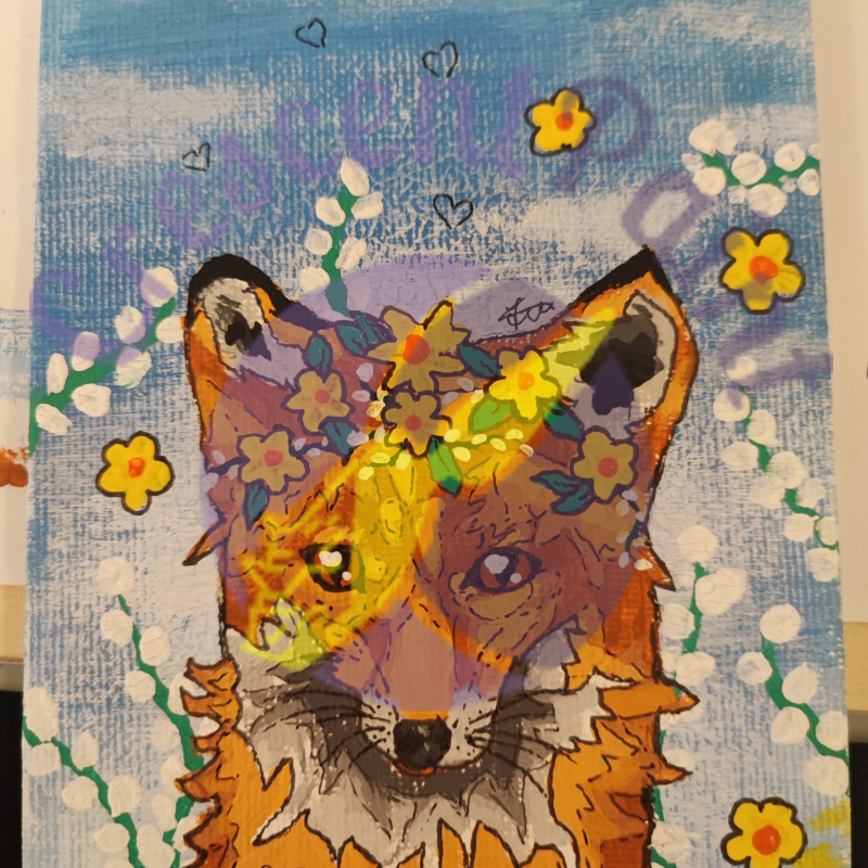A small orange fox wears a yellow flower crown with blue sky and branches of a weeping willow catkin in the background.