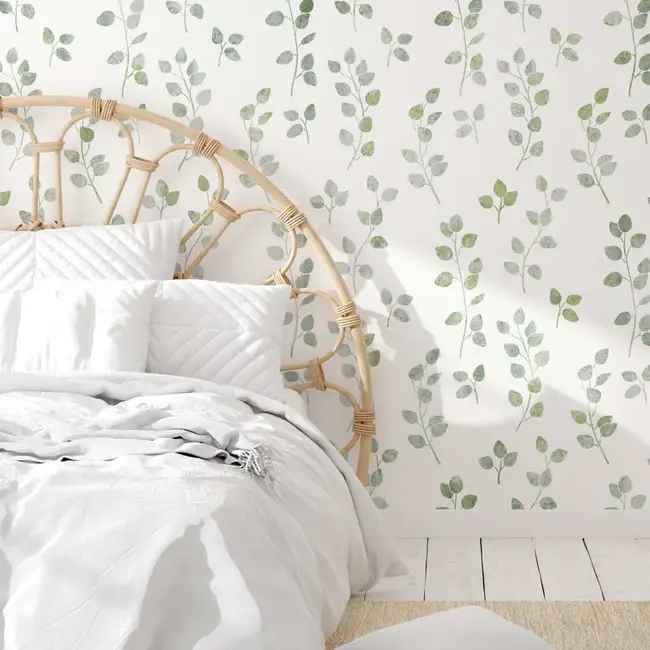 image of a part of a wicker bed against a white wall with wallpaper stencil of leaves in a light mossy green color