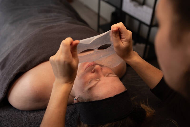 Huidspecialist brengt een gezichtsmasker aan tijdens een huidverbeterende behandeling in de salon in Den Haag.