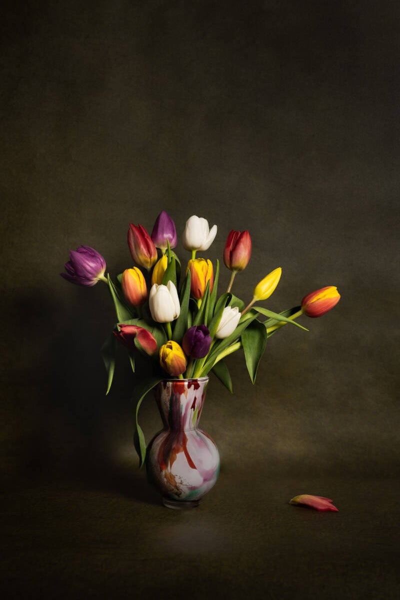 Stilleven met bont gekleurde tulpen in een glazen vaas. Laat je muren spreken met een prachtig verhaal vertellend stilleven van John van de Gazelle. Want, één beeld zegt meer dan duizend woorden.