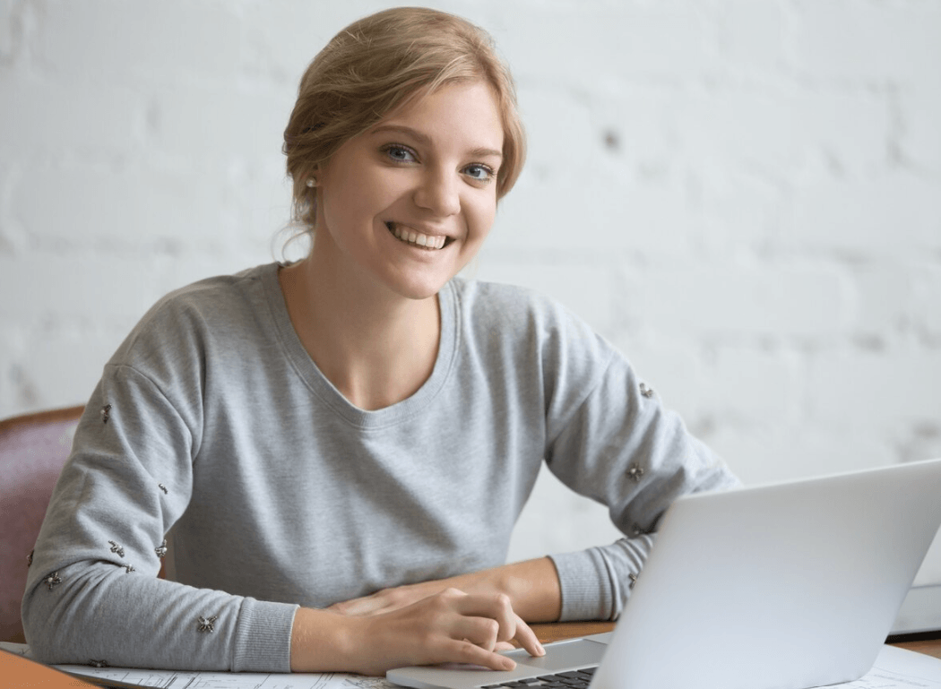 Smiling young woman at a laptop during online French tuition for GCSE, A-Level, and 13+ Common Entrance exam preparation.