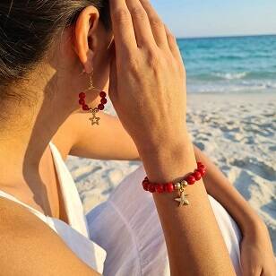 Model draagt handgemaakte rode kralenarmband en oorbellen van Resibe op het strand.