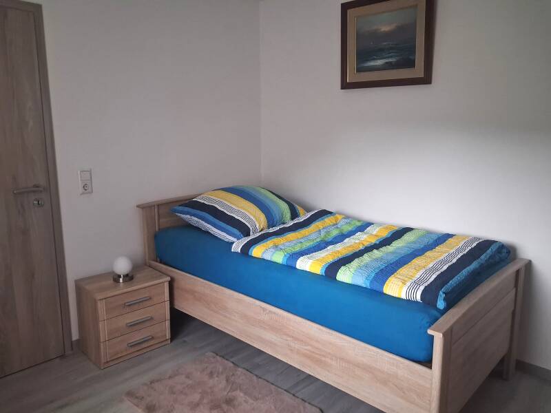das gemütliche Einzelzimmer mit Bett  und Schrank. An der Wand befindet sich ein Bild mit Meeresmotiv
