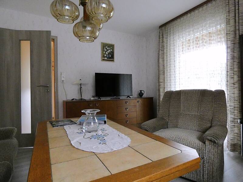 Das Wohnzimmer mit Flachbildschirm Tisch, Lampe, Sofa und Tür zum Flur und zu der überdachten Terrasse