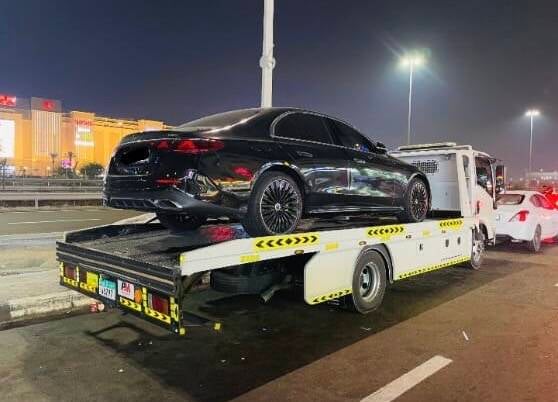 Nighttime 24/7 emergency car recovery flatbed tow truck with flashing amber lights assisting a driver in Al Khalidiya Abu Dhabi
