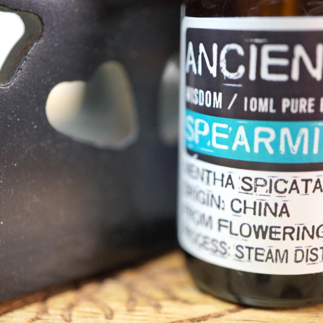 In een roze aroma brander ligt : 100% pure Spearmint, of groene munt, essentiële olie van Ancient Wisdom, 10 ml.