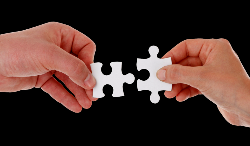 Zwei Hände, die jeweils ein weißes  Puzzlestück halten und diese zusammenfügen, symbolisieren Verbindung im Kontext von der kombinierten Sitzung als Jenseitskontakt und Geistführerkontakt mit Medium Jana Lorenz.