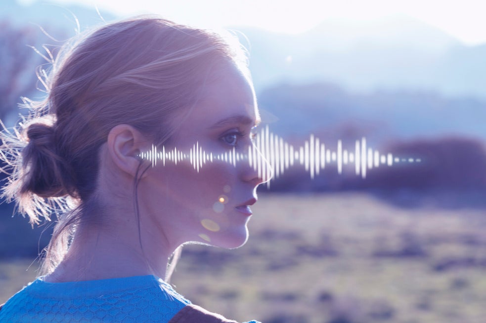Frau mit hochgestecktem Haar trägt ein Hörgerät im rechten Ohr, im Hintergrund Berglandschaft und stilisierte Schallwellen, Kontext Blog Mediumship & Research Institut für Medialität & Afterlife Forschung.