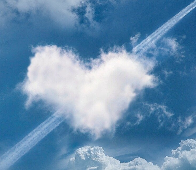 Eine herzförmige Wolke im Himmel, umgeben von weiteren Wolken und einem Kondensstreifen, Kontext Blog Mediumship & Research Institut für Medialität & Afterlife Forschung.