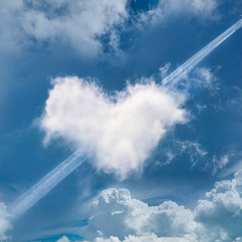 Eine herzförmige Wolke im Himmel, umgeben von weiteren Wolken und einem Kondensstreifen, Kontext Blog Mediumship & Research Institut für Medialität & Afterlife Forschung.