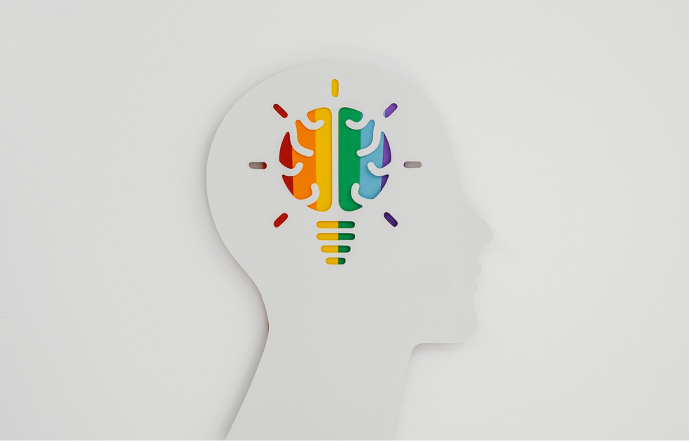 Silhouettenprofil eines Kopfes mit einer bunten Glühbirne in Form eines Gehirns im Inneren, symbolisiert Optimismus , Kontext Blog Mediumship & Research Institut für Medialität & Afterlife Forschung.
