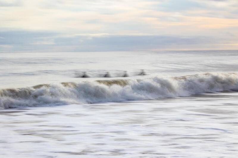 Verschwommene Silhouetten von vier Personen, die im Meerwasser stehen, vor einem wellenbewegten Ozean unter bewölktem Himmel, , passend zum Thema Geistführerkontakt  mit Medium Jana Lorenz