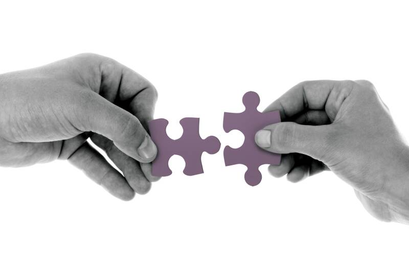 Zwei Hände, die jeweils ein violettes Puzzlestück halten und diese zusammenfügen, symbolisieren Verbindung im Kontext von der kombinierten Sitzung als Jenseitskontakt und Geistführerkontakt mit Medium Jana Lorenz.