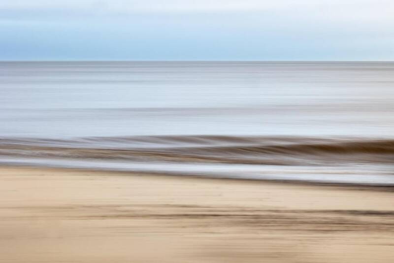 Weicher, verschwommener Blick auf einen ruhigen Strand mit Sand im Vordergrund und ruhigem Meer im Hintergrund, passend zum Thema Geistführerkontakt mit Medium Jana Lorenz