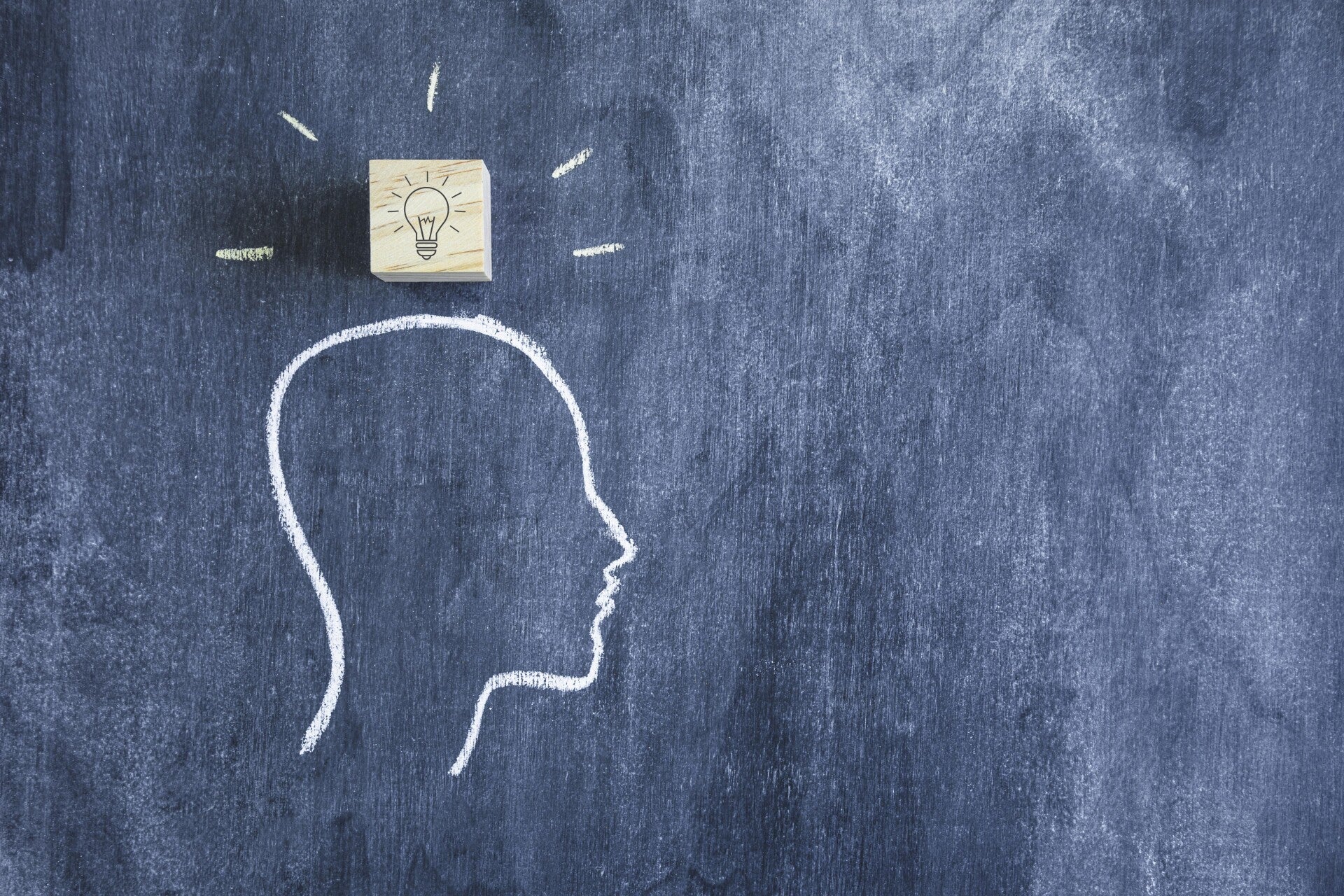 Eine Kreidezeichnung eines Kopfprofils auf einer Tafel, mit einem Holzblock mit einer Glühbirne darüber, Kontext Blog Mediumship & Research Institut für Medialität & Afterlife Forschung.