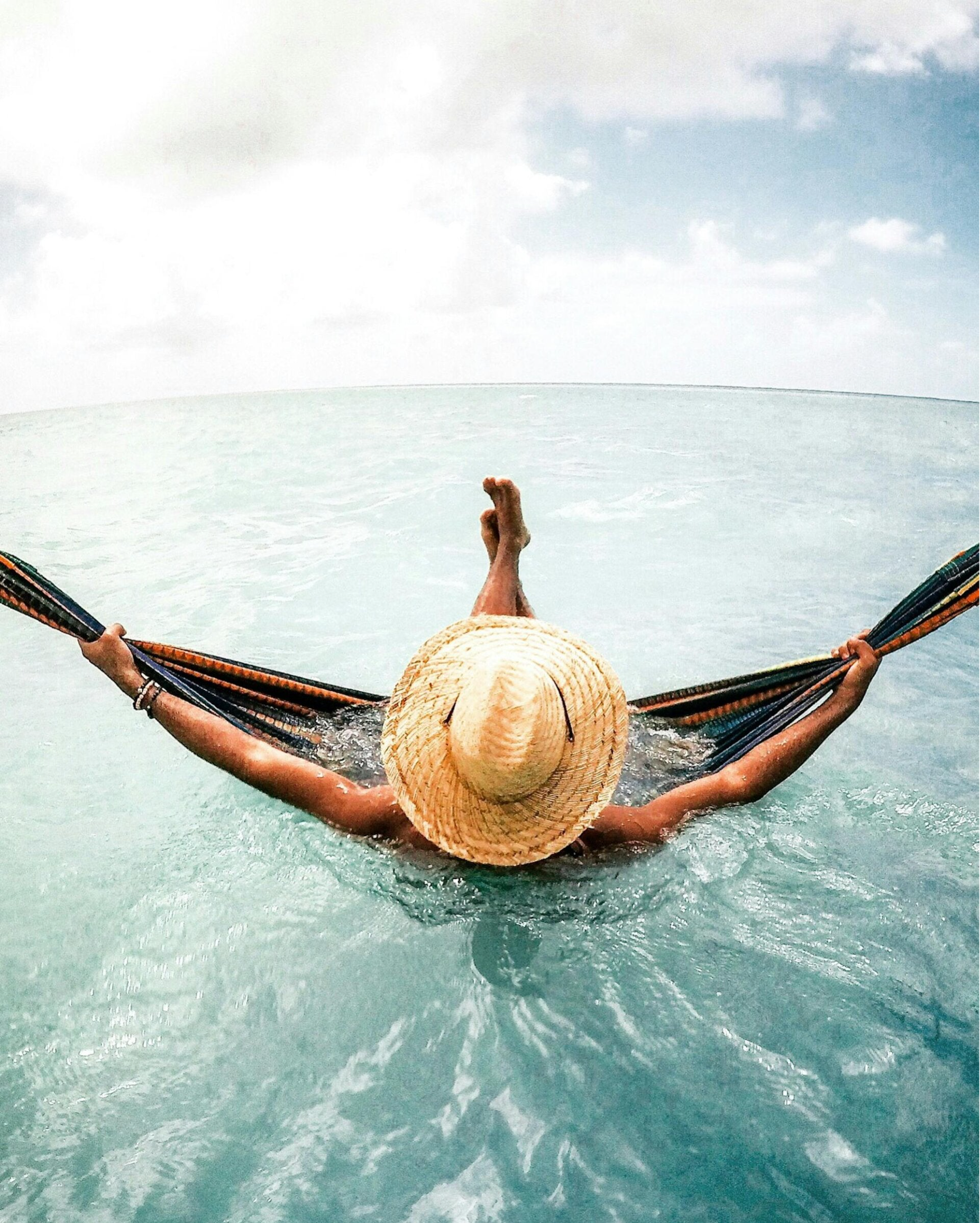 homme ou femme avec un chapeau de paille qui se balance  dans un hamac dans l'eau